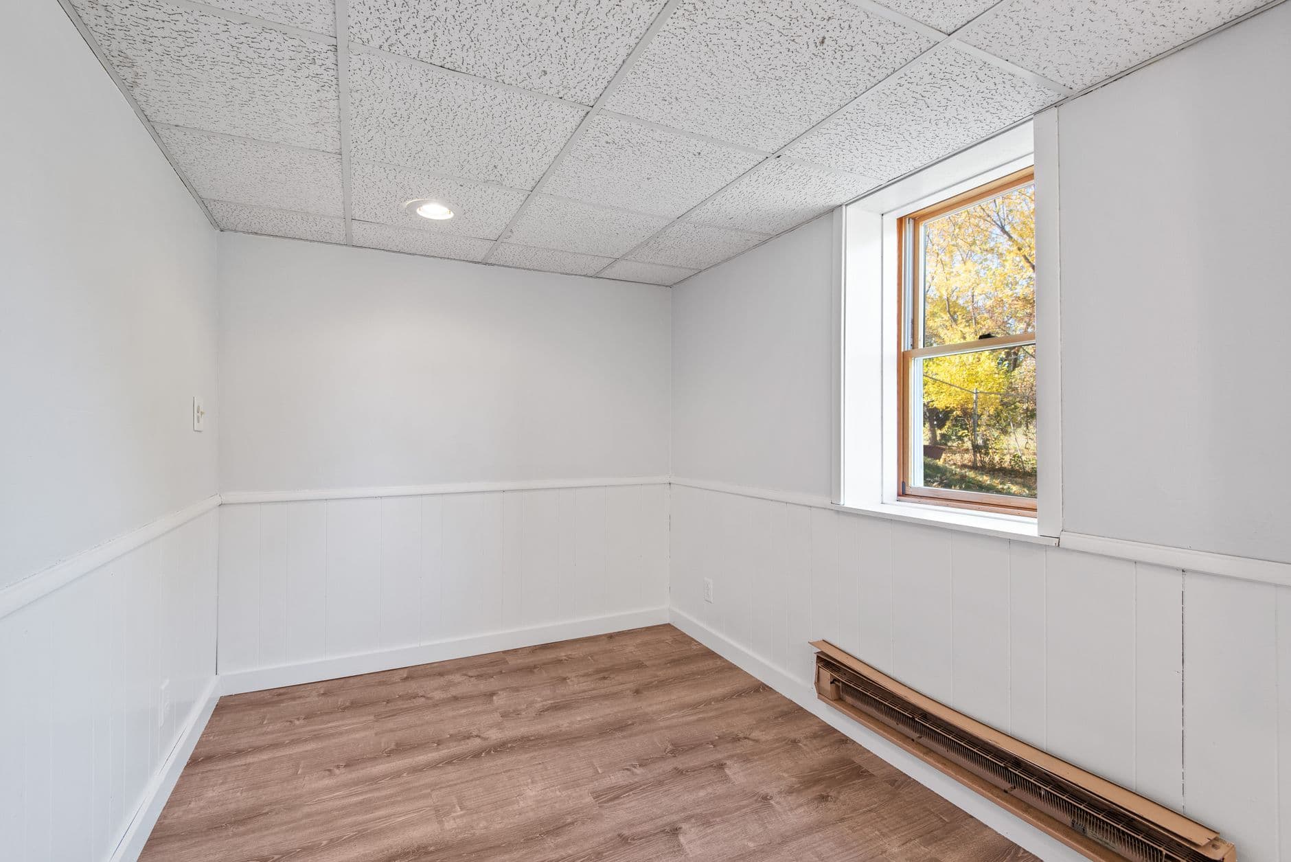 Lege kamer met een systeemplafond, witte lambrisering en een raam met zicht op gele bomen