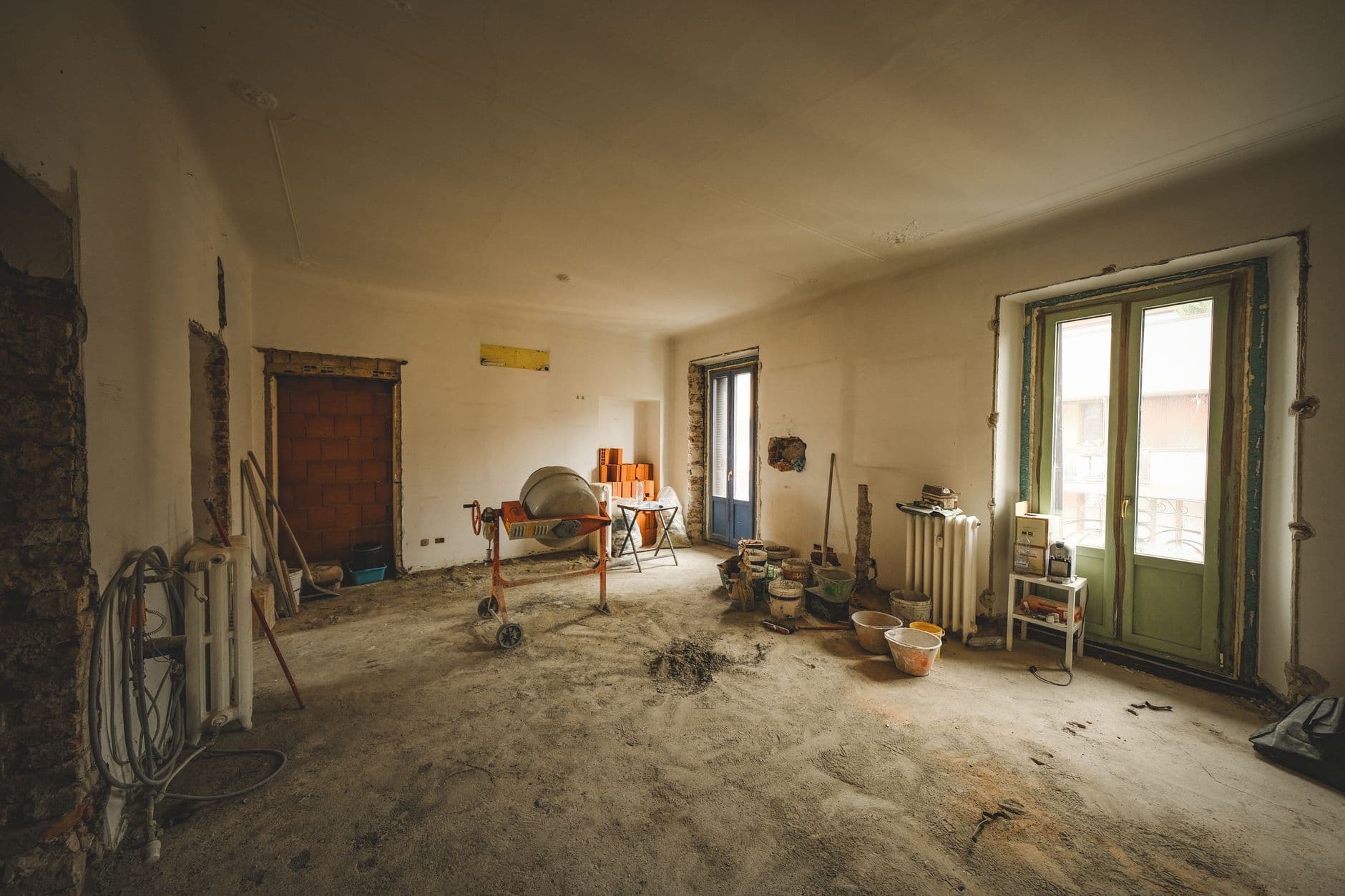 Ruime kamer in verbouwing met een betonmolen, emmers, oude radiatoren en groene deuren