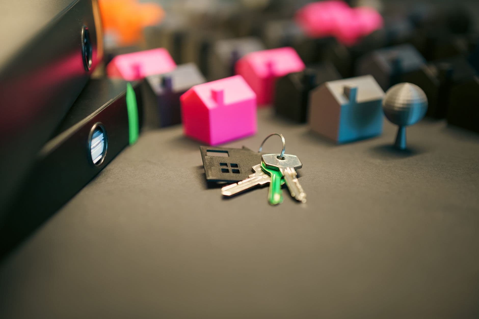Sleutelbos met een zwart sleutelhangertje in huisvorm, voor roze en grijze modelhuisjes, links twee donkere ordners