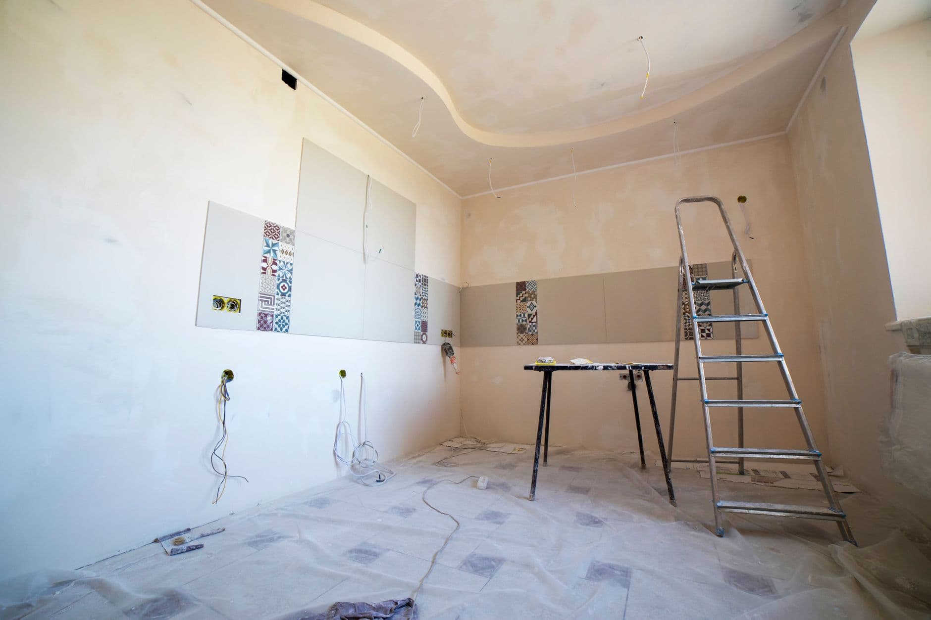 Kamer in renovatie met losse stroomdraden, afdekfolie op de vloer en een aluminium trapladder