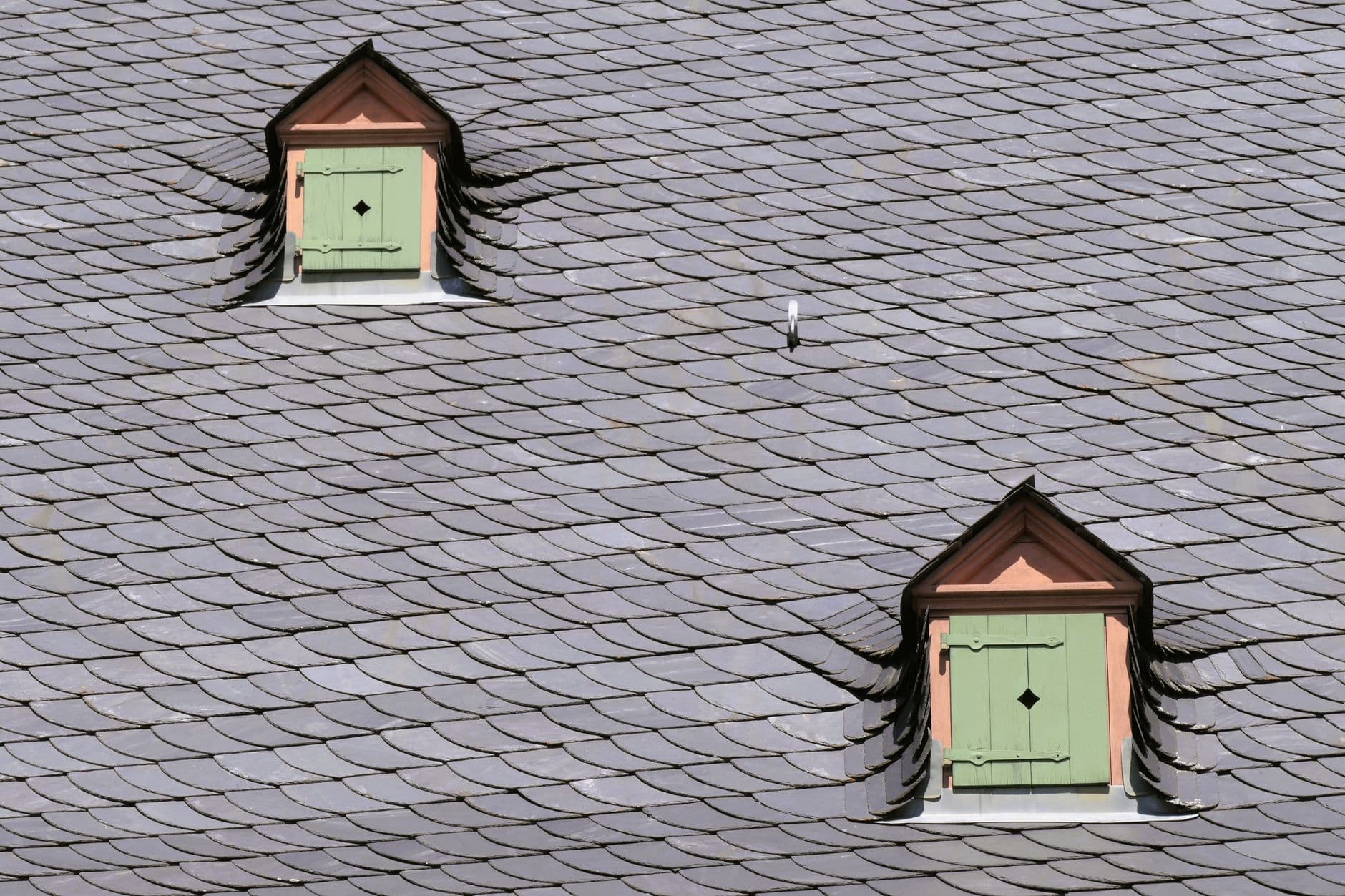 Grijs leien dak in schubpatroon met twee kleine dakkapellen, elk met een groen luik