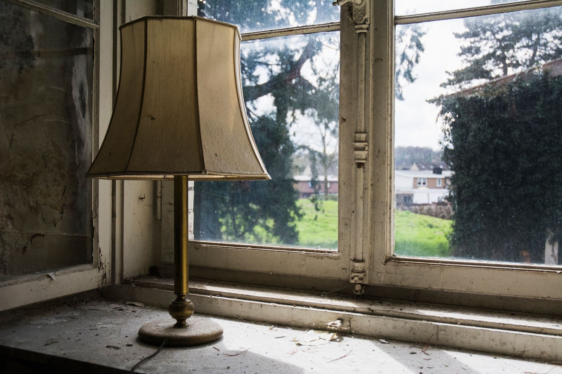 Oude tafellamp op een stoffige vensterbank, voor een houten raamkader met afbladderende verf