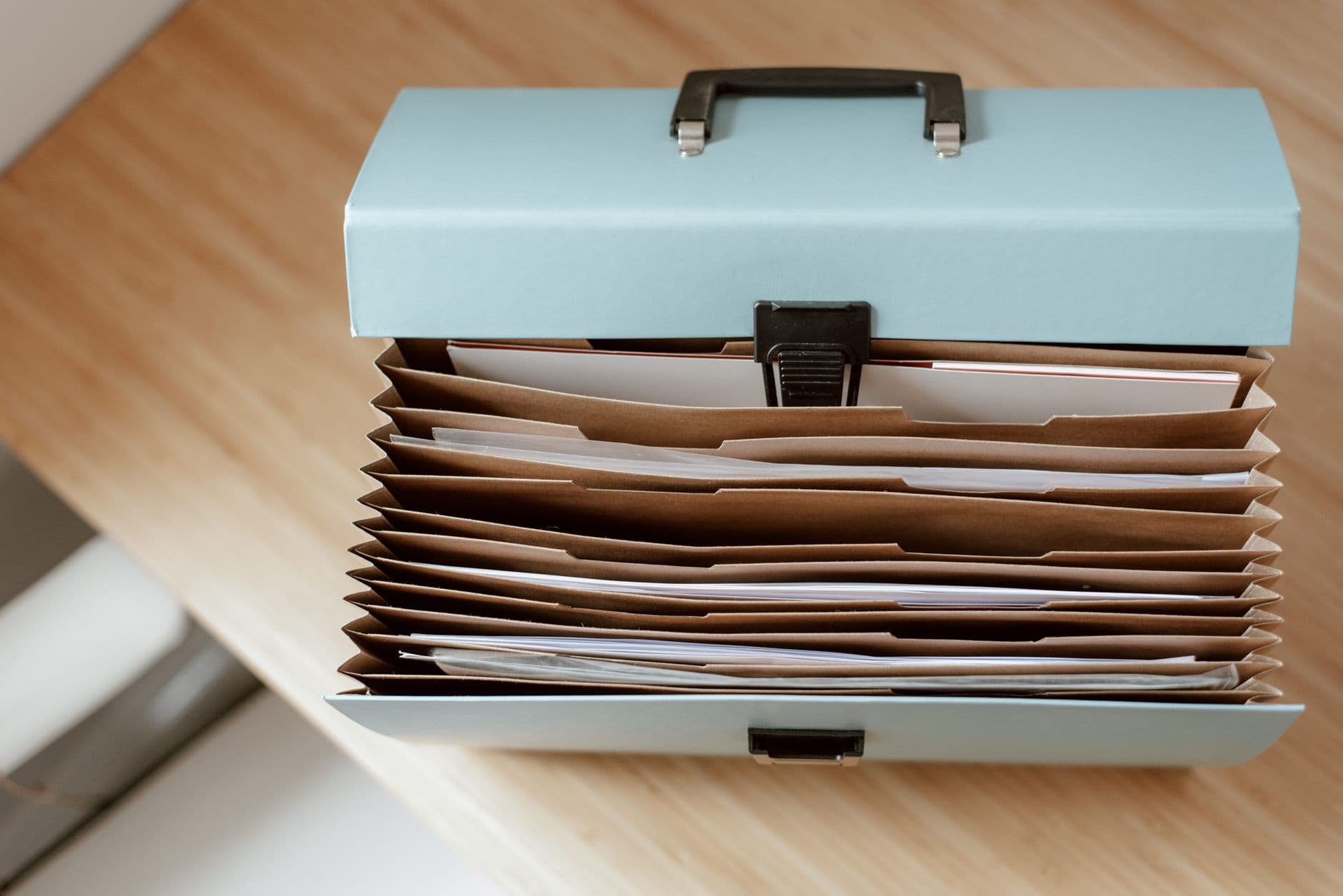 Lichtblauwe harmonicamap met handvat en vakken vol papieren op een houten tafel