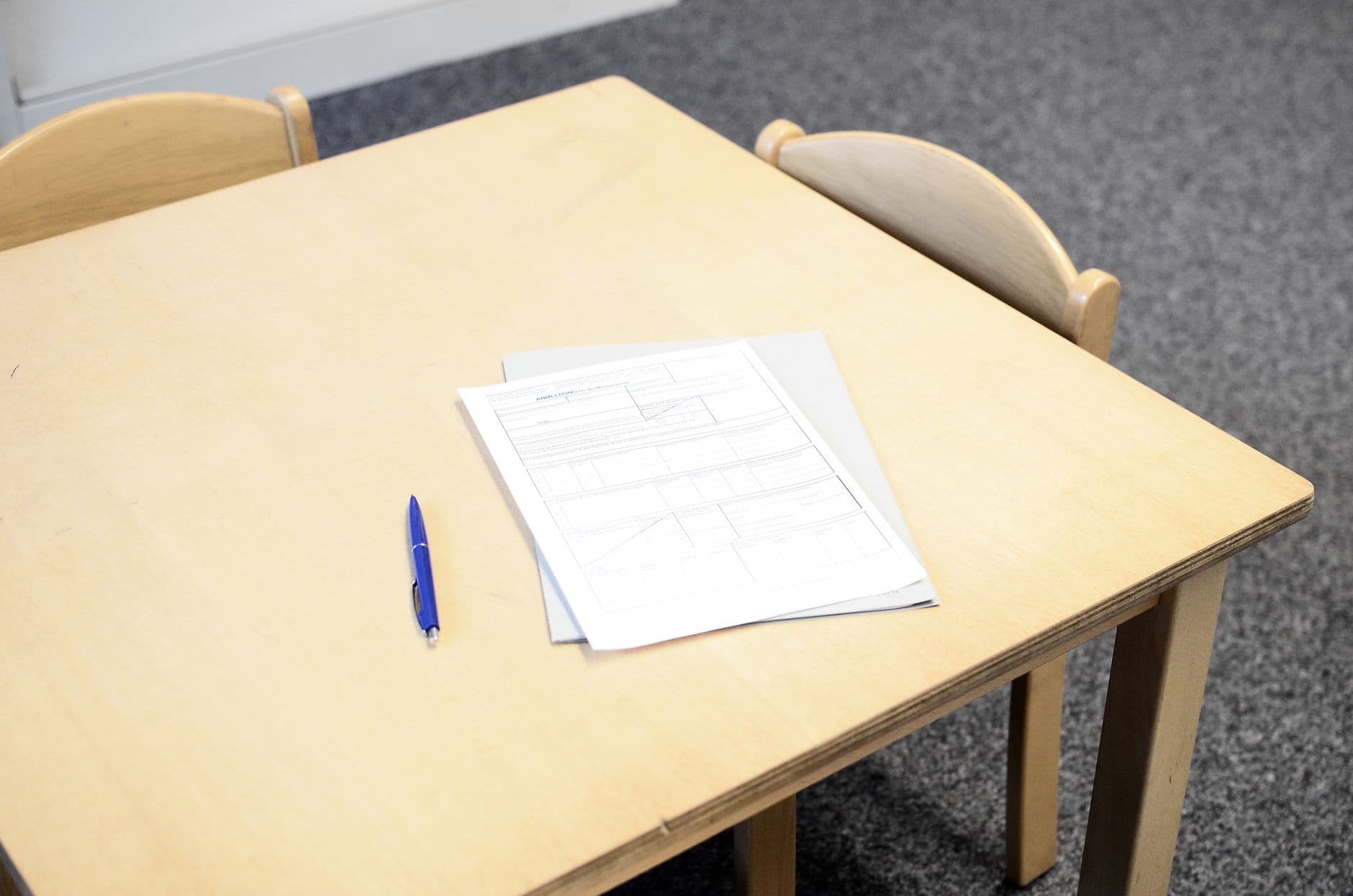 Lichthouten tafel met een blauwe balpen en een formulier op een grijze map