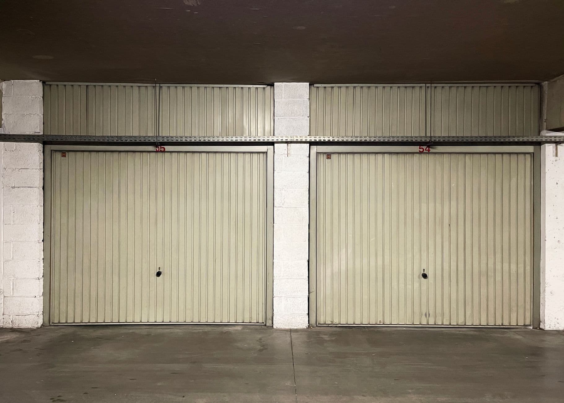 Twee gesloten garageboxen met poorten van geribd metaal tussen witte betonblokken