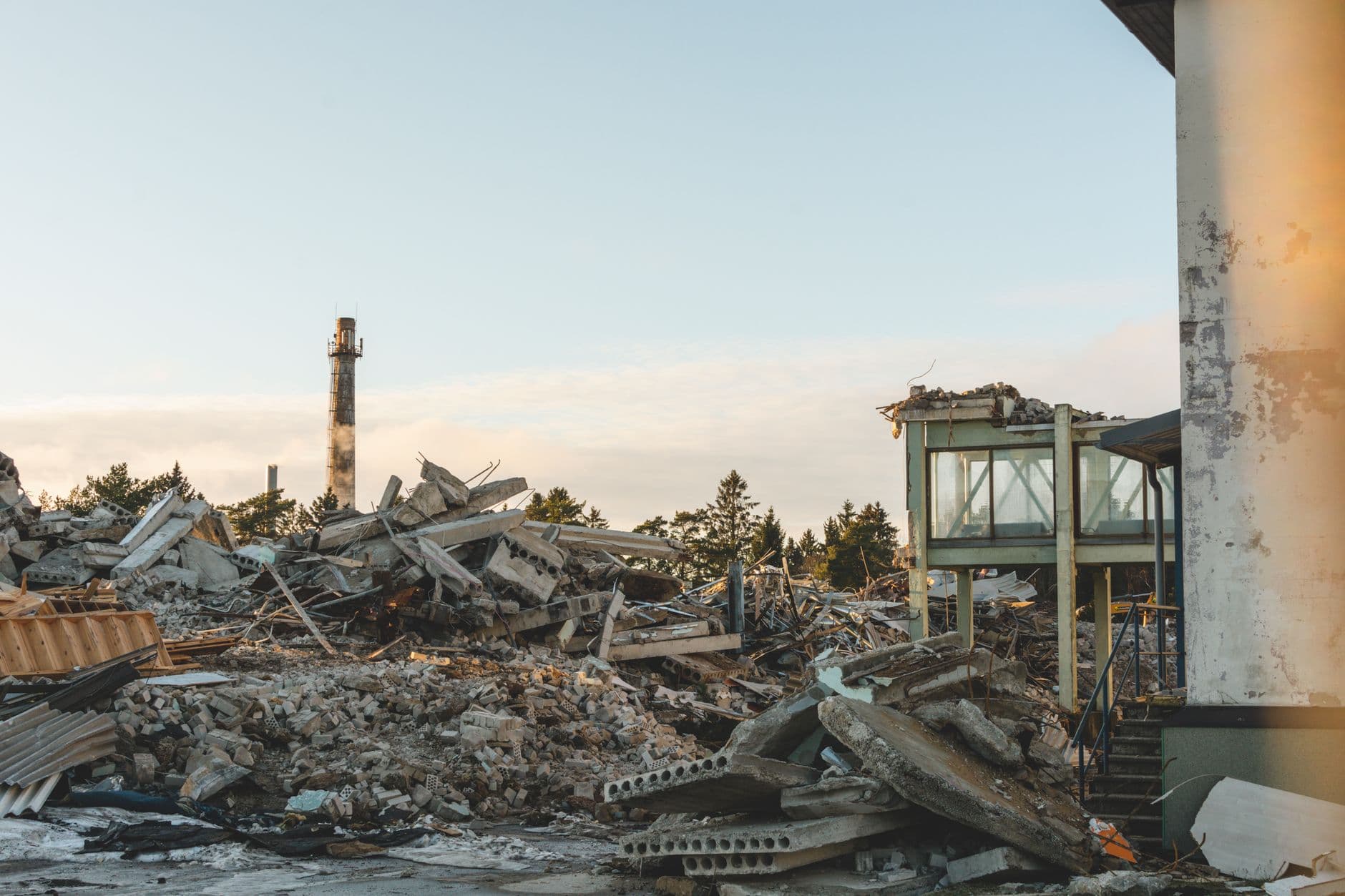 Sloopterrein vol betonpuin en gebroken welfsels, met in de verte een hoge schoorsteen