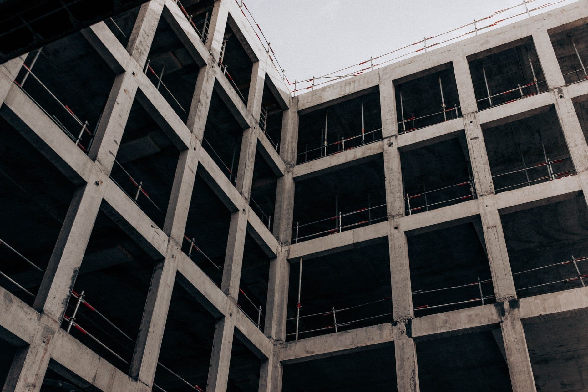 Ruwbouw van een betonnen gebouw van onderuit gezien, met open verdiepingen en werfleuningen