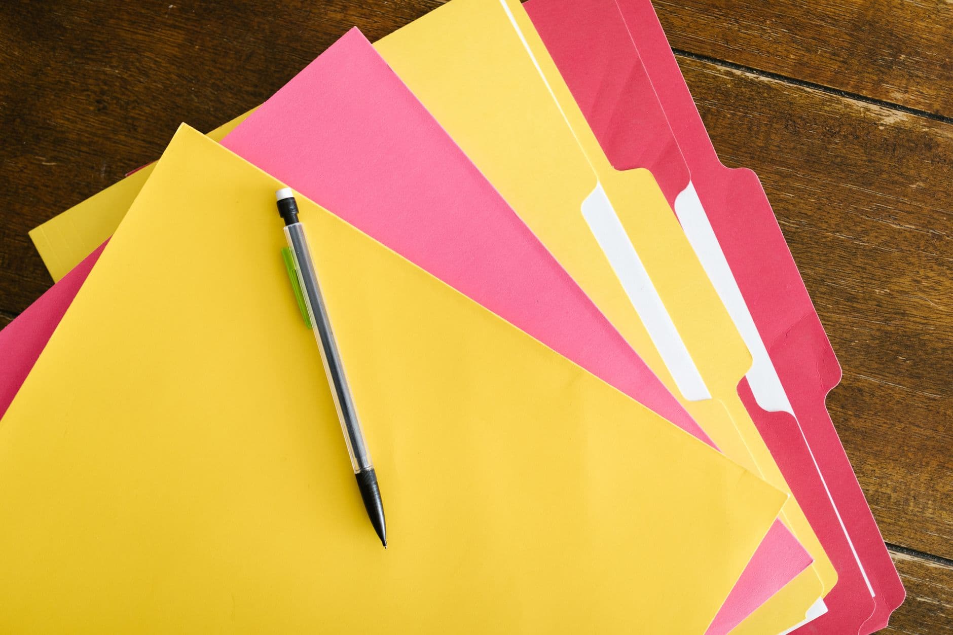 Gele en roze dossiermappen met een vulpotlood op een houten tafel