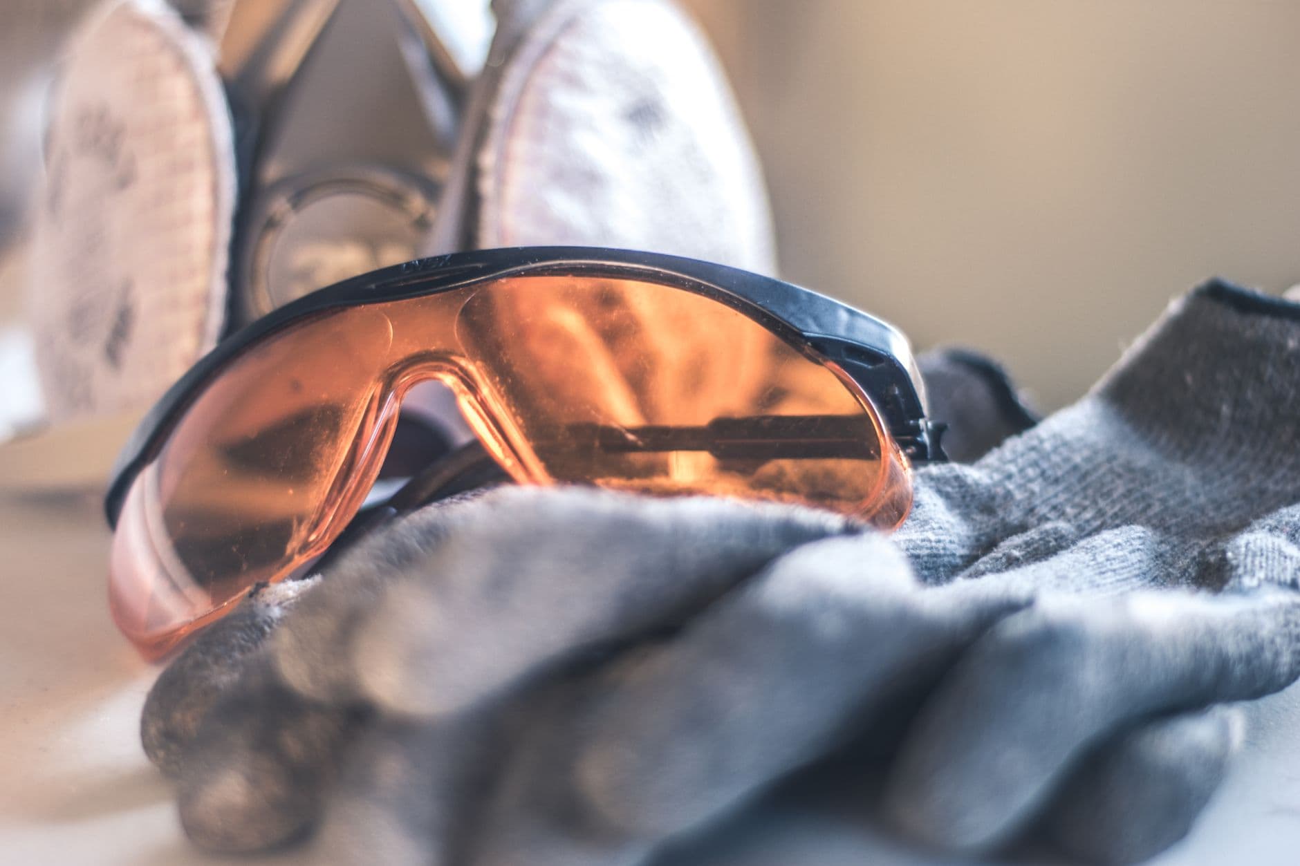 Veiligheidsbril met oranje glazen op grijze werkhandschoenen, daarachter een halfgelaatsmasker met twee filters